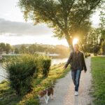 Young man takes his beloved dog for a walk in the park at sunset